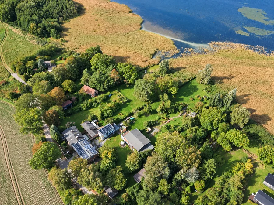 Luftaufnahme des WeLa-Areals mit Haupt- und Nebengebäuden, Photovoltaikflächen, Garten und angrenzendem Bodden.